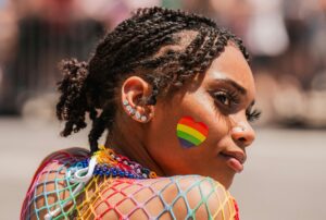 Black LGBTQIA+ woman with a rainbow heart on her right cheek lookin over her shoulder to the right